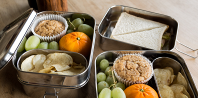grapes, crisps, sandwich, cupcake, and a orange in three metal lunch boxes
