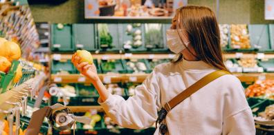Woman in face mask holding lemon in supermarket aisle