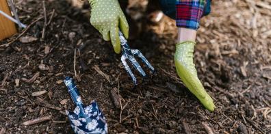 Zoomed in on green gardening gloves holding a trowel over compost pile