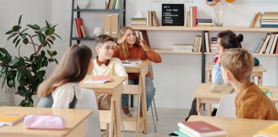 Kids sat at wooden desks in white classroom.