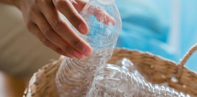 Hand holding empty plastic bottle over wicker basket full of plastic bottles